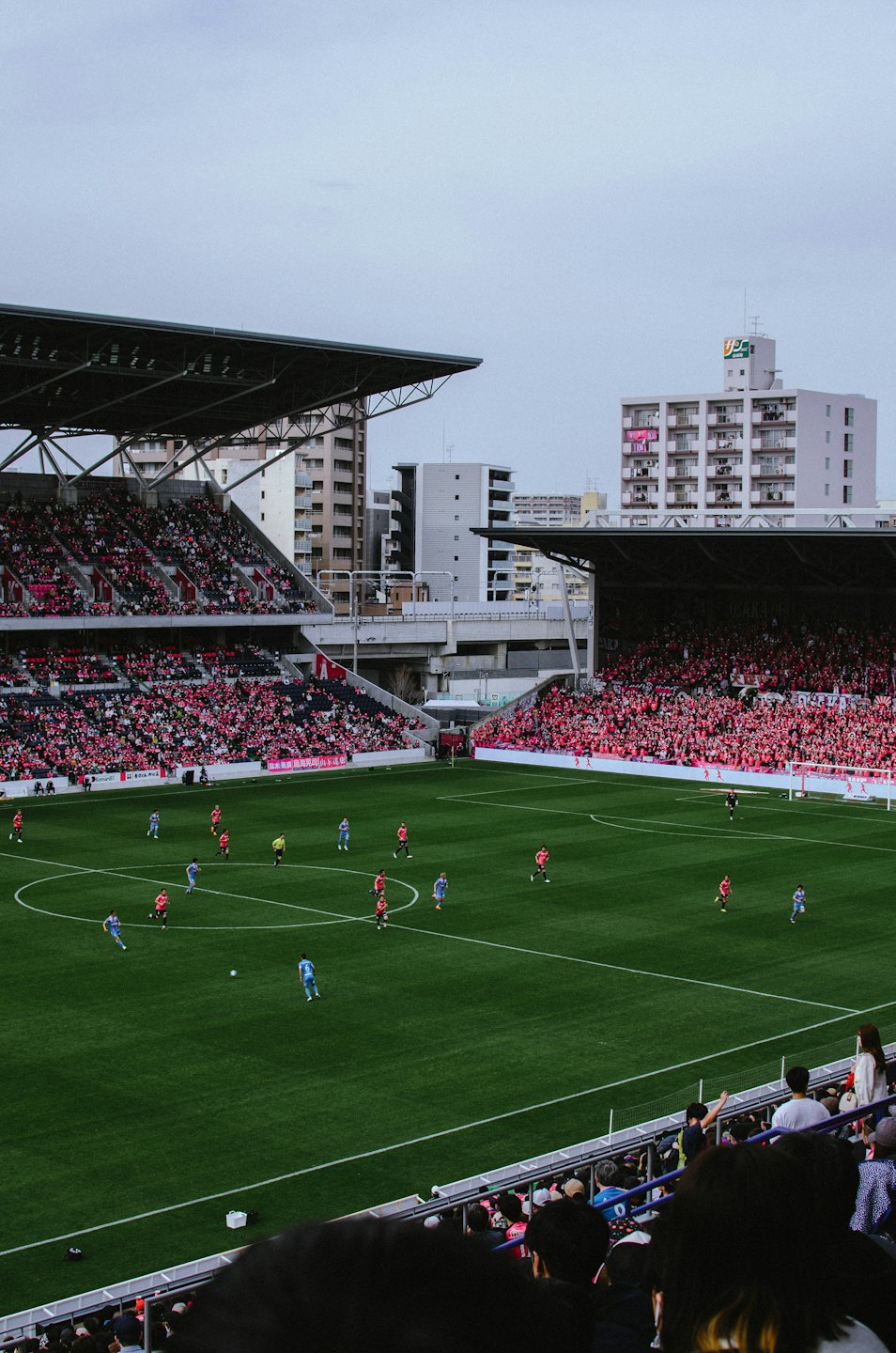 Piłkarze rywalizują na boisku stadionu przed budynkami miejskimi.